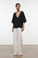 Black studio tee with deep V-neck and wide short sleeves worn with light trousers