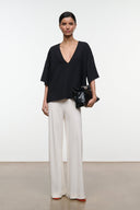 Black studio tee with deep V-neckline and loose short sleeves worn with light trousers