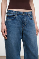 A close-up of a person wearing blue wide-leg jeans with a dark brown ribbed top, cropped from the chest down against a plain light background.