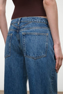 Close-up back view of a person wearing medium-wash blue denim jeans with a dark brown ribbed top, showing the back pockets and waistband details.