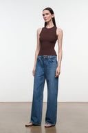 A woman modeling a sleeveless dark brown ribbed top and wide-leg blue jeans against a plain white studio background.
