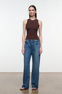 A woman modeling a sleeveless dark brown mock-neck top and wide-leg blue jeans against a plain white studio background.