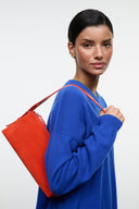 Orange shoulder bag with structured shape and top handles, held at side
