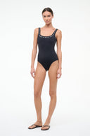 Black one-piece swimsuit worn with black sandals; silver eyelet trim at neckline