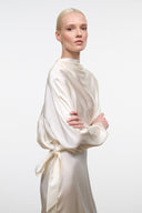 Ivory silk midi dress with draped high neckline, long sleeves, and tie-waist sash