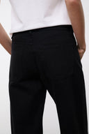 Black relaxed jeans close-up with stitched seam and rear pocket detail, wide leg