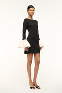 Black long-sleeve mini dress with ivory ruffle cuffs, angled view