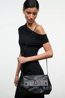 Black convertible shoulder bag with ruched top and front flap, worn with long strap