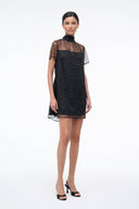 Mini shift dress in dark onyx with mock neck and sheer star-pattern sleeves, short straight hem.