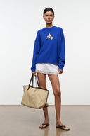 Blue crewneck sweater worn with lace shorts; beach-themed embroidered patch