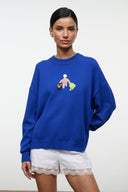 Blue knit sweater with crew neck; beach-themed embroidered patch on chest