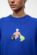 Close-up of beach-themed embroidered patch on the chest of a blue knit sweater