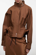 Brown cropped jacket with stand collar, front zip, button snaps, flap pockets, drawstring hem