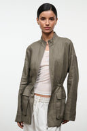 Olive linen jacket with stand collar, front zipper, side flap pockets, and gathered cuffs