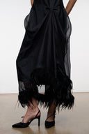 Black sleeveless dress with draped skirt and feather fringe hem, paired with black heels