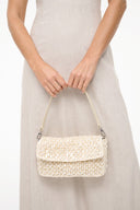Cream woven shoulder bag worn at waist height with flap closure