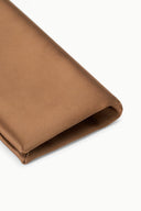 Tan leather clutch bag corner close-up with folded edge and seam detailing.