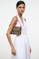Cheetah-print flap shoulder bag with red strap and silver buckle, worn with white dress