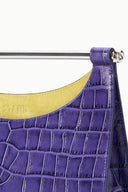 Close-up of purple crocodile-pattern clutch with silver bar latch and edge seam