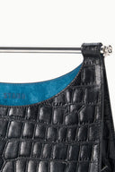 Black croc-embossed clutch close-up with metal top bar clasp and blue interior lining.