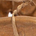 Ceramic sculpture close-up of tan strap with small grommets and twine tying stitches