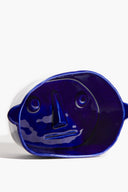 Small ceramic dog bowl, glossy blue with raised dog-face pattern (front view)