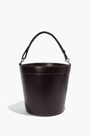 Dark brown leather bin with arched carry handles, stitched rim and smooth bucket silhouette.