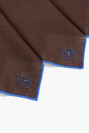 Linen napkin corner detail in espresso brown with blue trim and elephant emblem