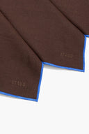 Dark brown linen placemat corners with blue edging and 'STAUD' label