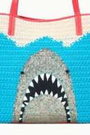 Front of blue crocheted tote bag with shark graphic and cream zigzag trim, red handles