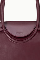 Burgundy leather bag close-up of STAUD logo on curved top pocket