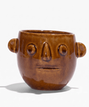 Ceramic candle pot with warm brown glaze and carved smile; circular eye details and handles
